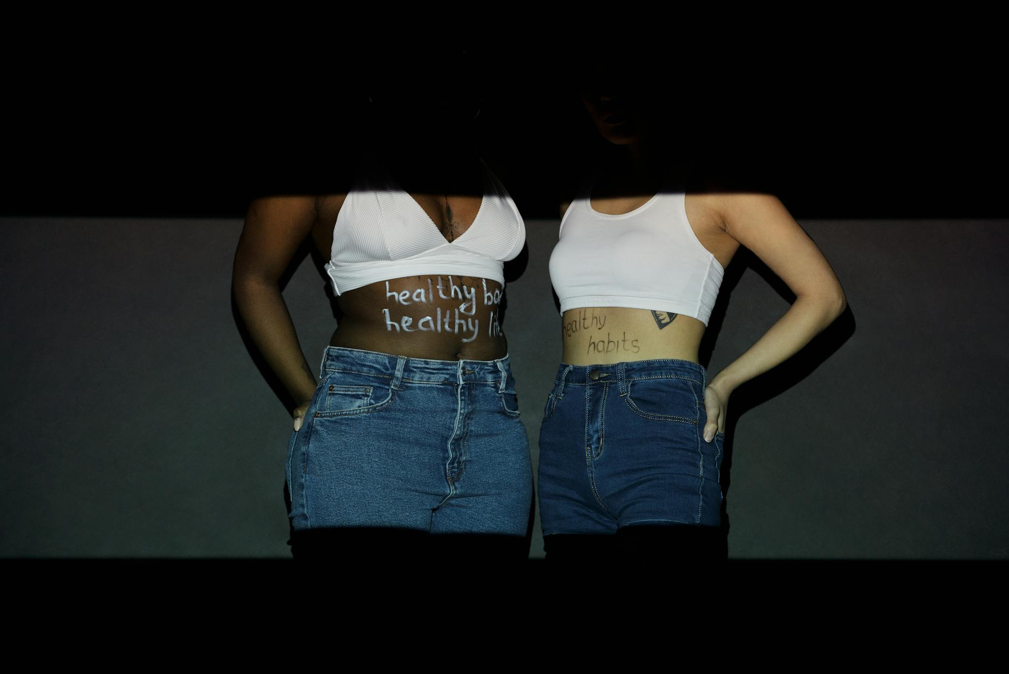 Two women promote healthy habits with inspiring text on their bodies.